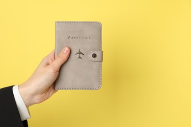 Woman holding passport in bright cover on yellow background, closeup. Space for text