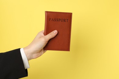 Photo of Woman holding passport in bright cover on yellow background, closeup. Space for text