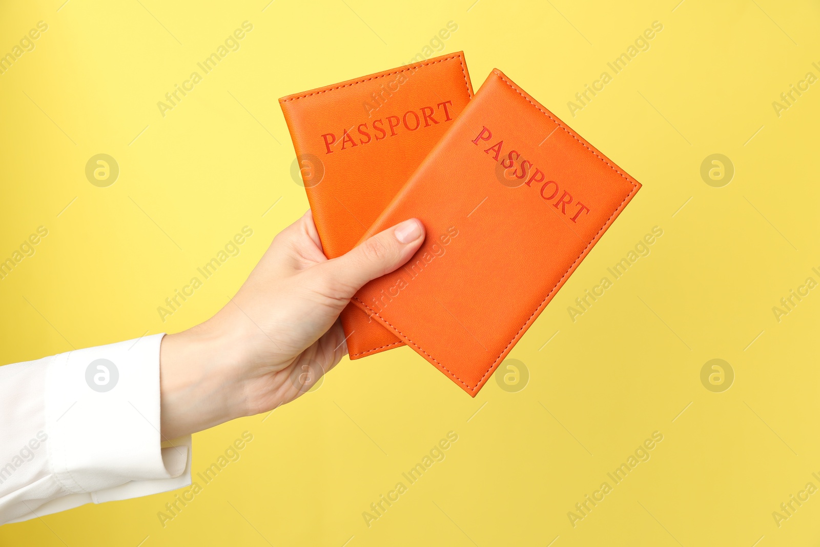 Photo of Woman holding passports in bright covers on yellow background, closeup