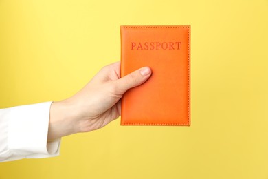 Photo of Woman holding passport in bright cover on yellow background, closeup