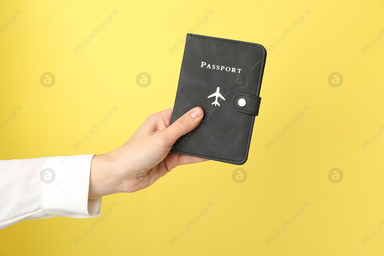 Photo of Woman holding passport in bright cover on yellow background, closeup