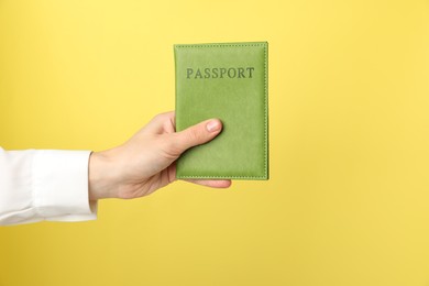 Photo of Woman holding passport in bright cover on yellow background, closeup