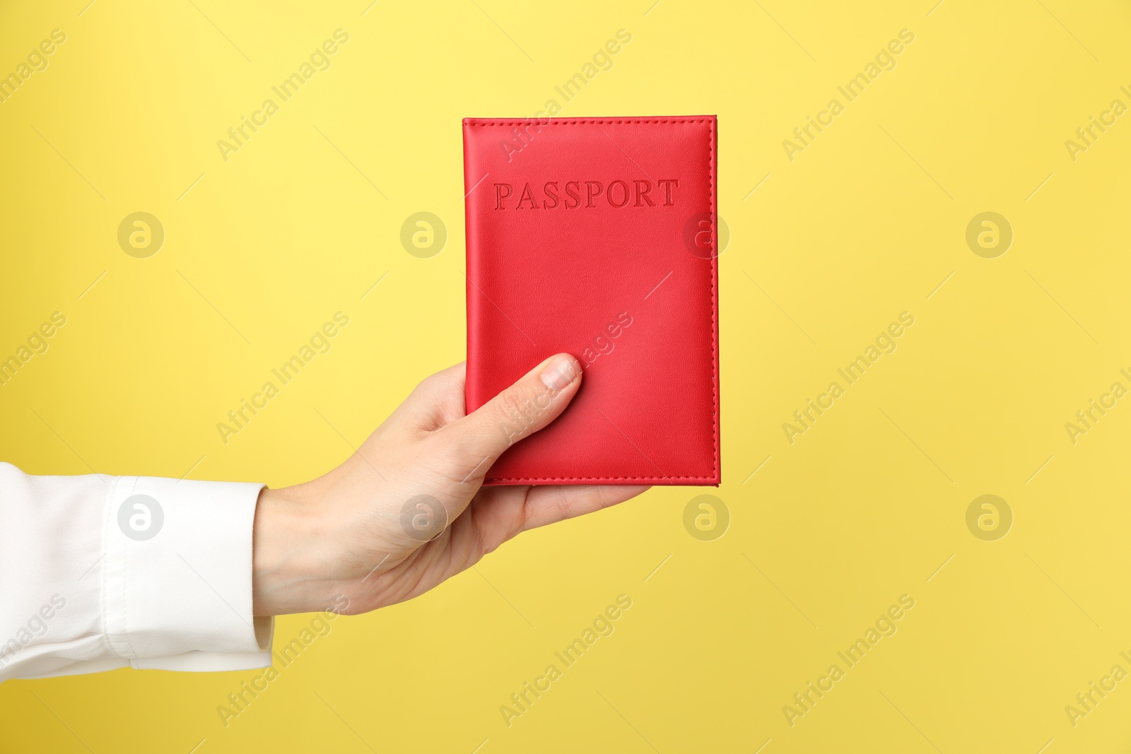 Photo of Woman holding passport in bright cover on yellow background, closeup