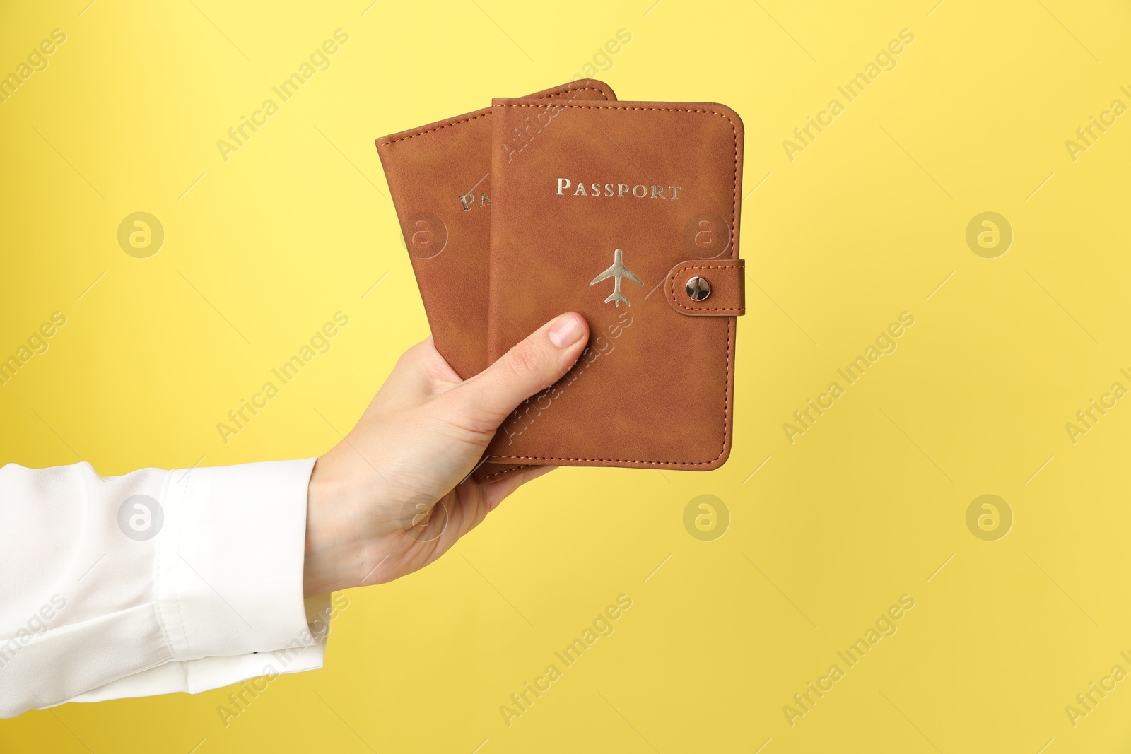 Photo of Woman holding passports in bright covers on yellow background, closeup