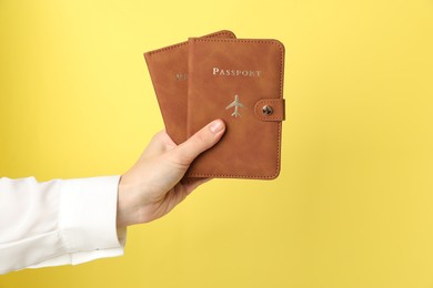 Photo of Woman holding passports in bright covers on yellow background, closeup