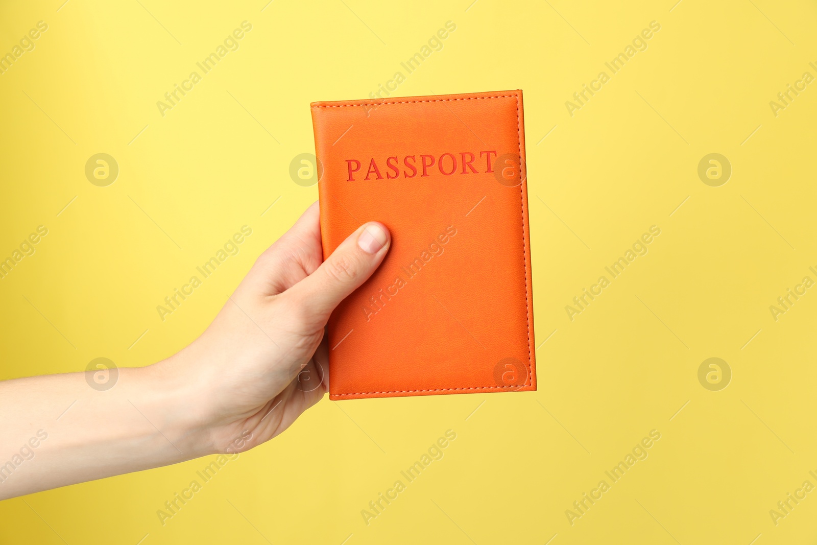 Photo of Woman holding passport in bright cover on yellow background, closeup