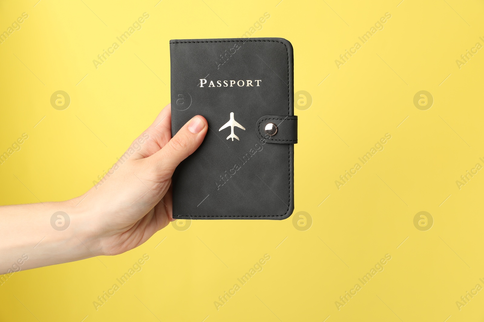 Photo of Woman holding passport in bright cover on yellow background, closeup