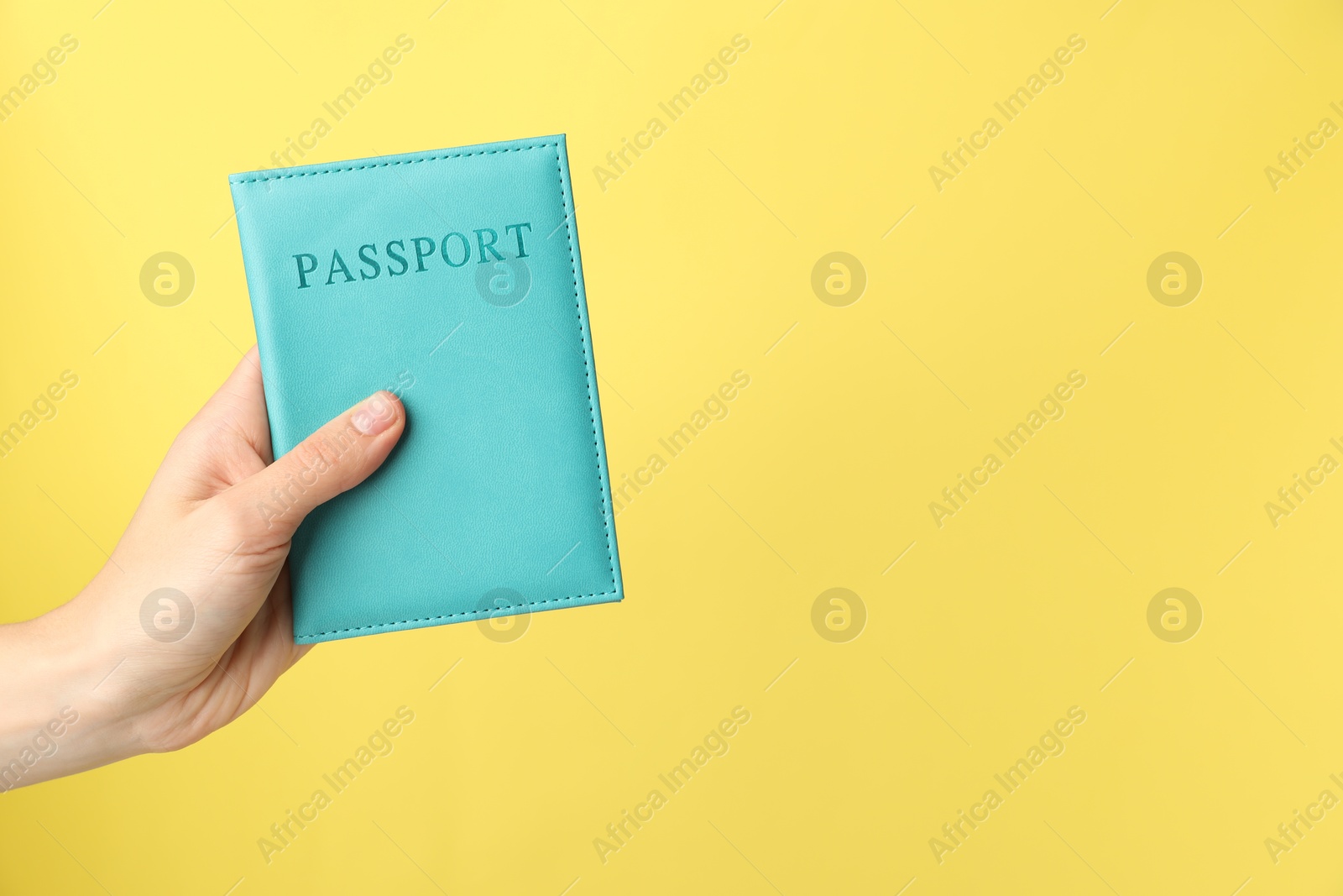 Photo of Woman holding passport in bright cover on yellow background, closeup. Space for text