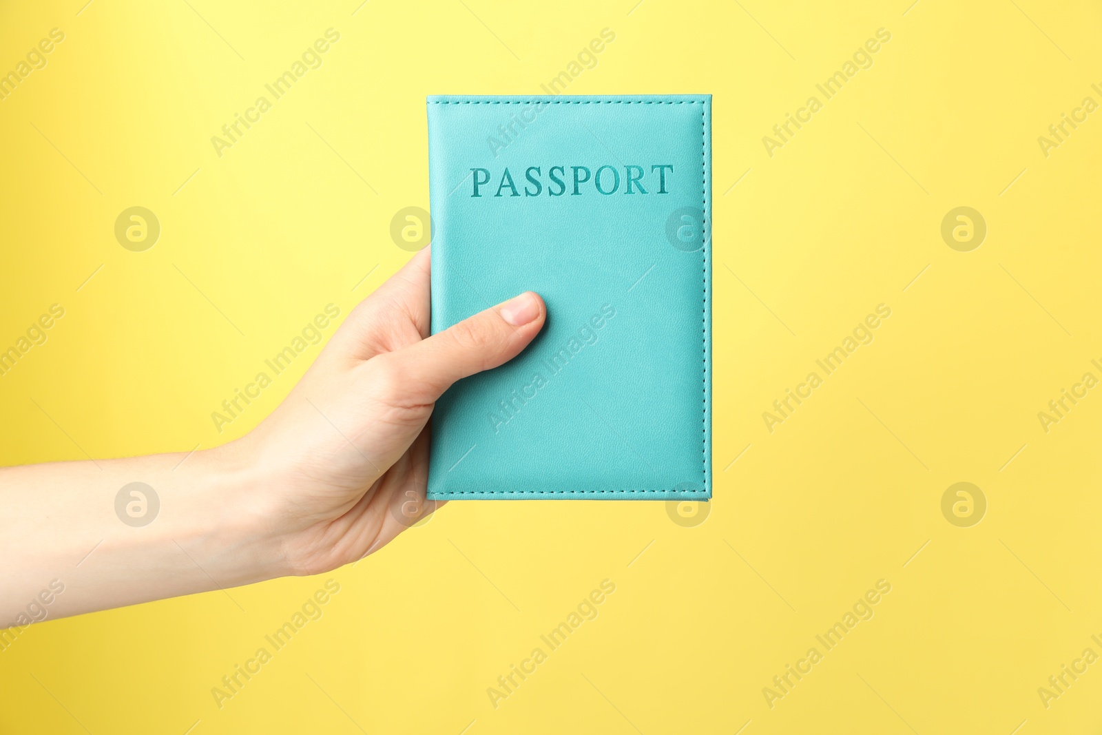 Photo of Woman holding passport in bright cover on yellow background, closeup