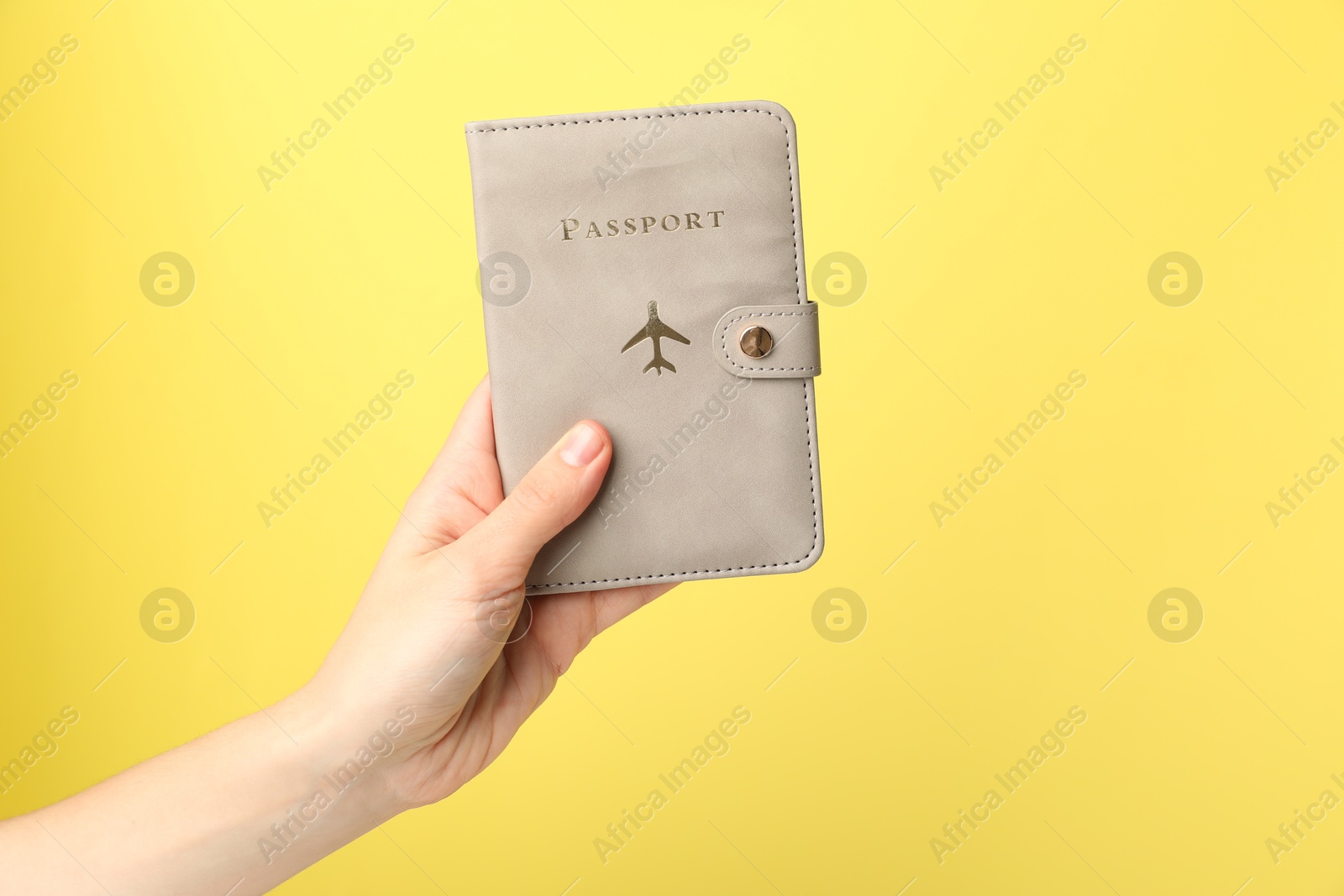 Photo of Woman holding passport in bright cover on yellow background, closeup