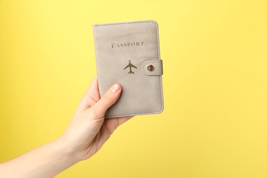 Photo of Woman holding passport in bright cover on yellow background, closeup