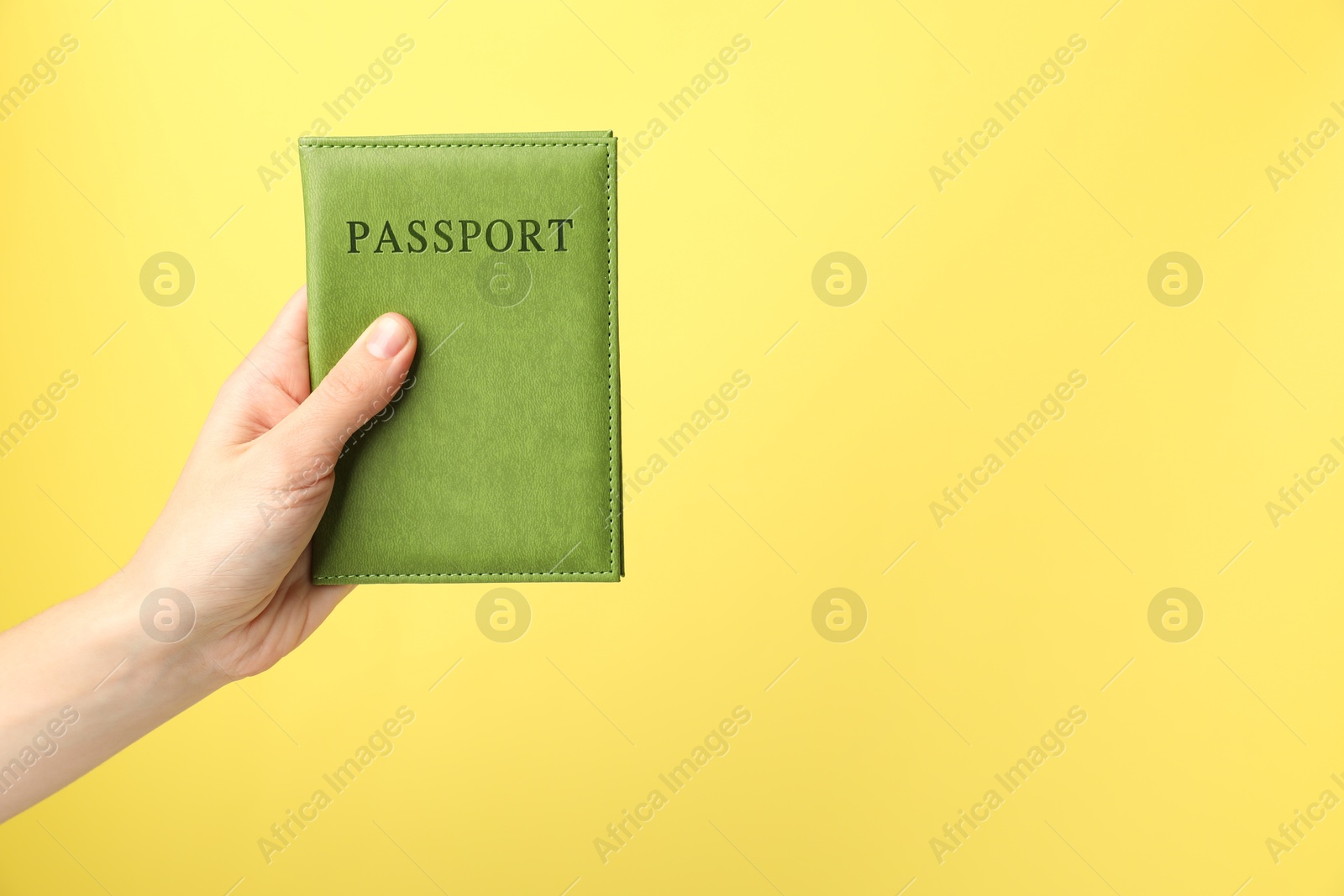 Photo of Woman holding passport in bright cover on yellow background, closeup. Space for text