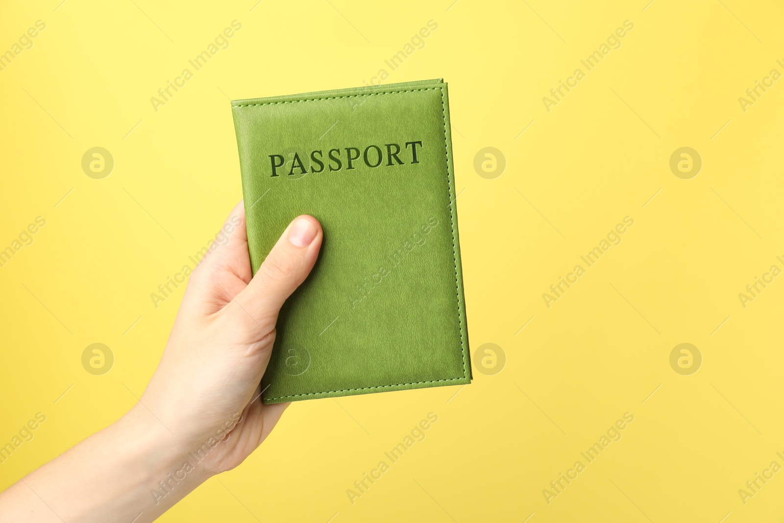 Photo of Woman holding passport in bright cover on yellow background, closeup