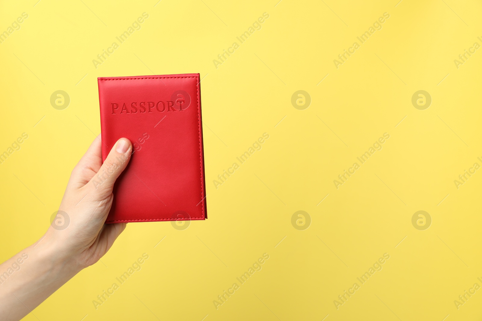 Photo of Woman holding passport in bright cover on yellow background, closeup. Space for text