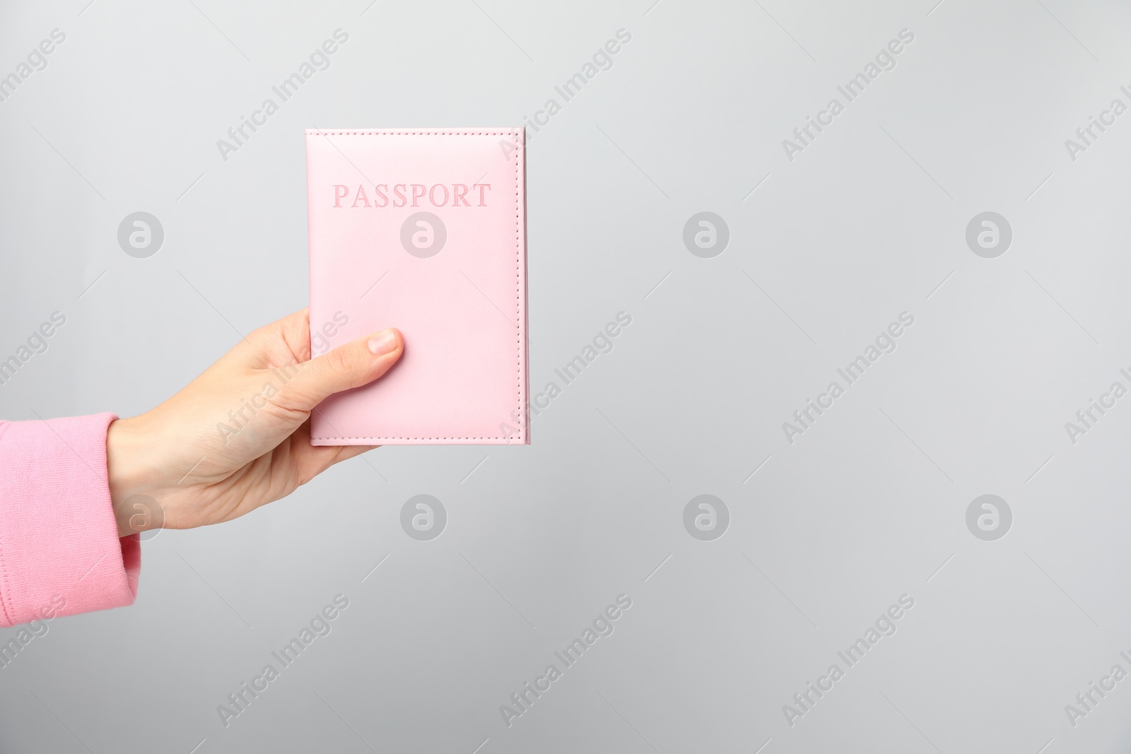 Photo of Woman holding passport in bright cover on grey background, closeup. Space for text