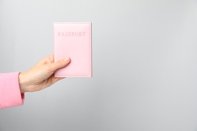 Photo of Woman holding passport in bright cover on grey background, closeup. Space for text