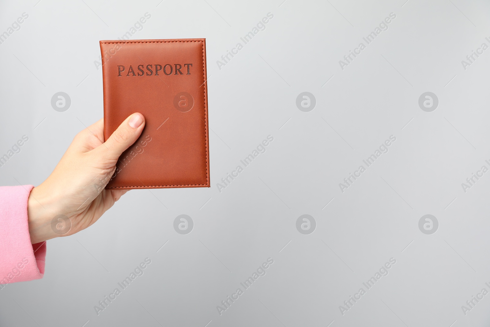 Photo of Woman holding passport in bright cover on grey background, closeup. Space for text