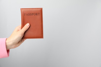 Photo of Woman holding passport in bright cover on grey background, closeup. Space for text