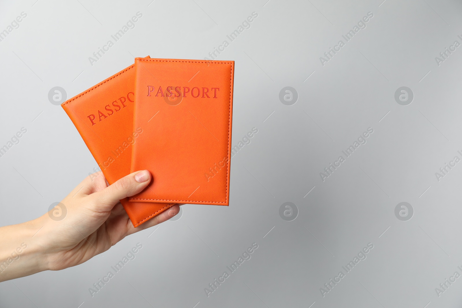 Photo of Woman holding passports in bright covers on grey background, closeup. Space for text