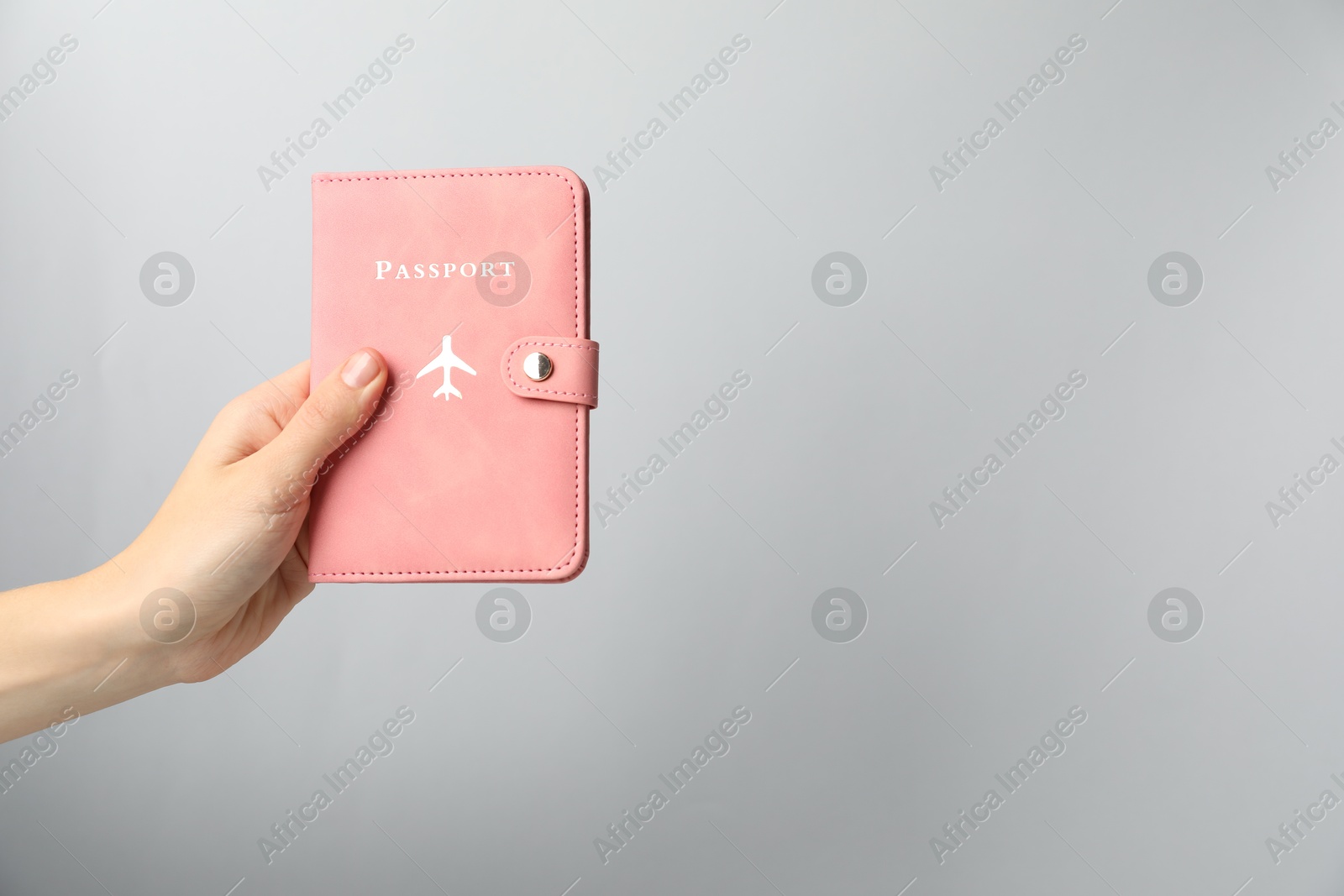 Photo of Woman holding passport in bright cover on grey background, closeup. Space for text