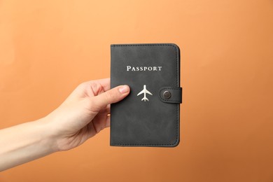 Photo of Woman holding passport in bright cover on orange background, closeup