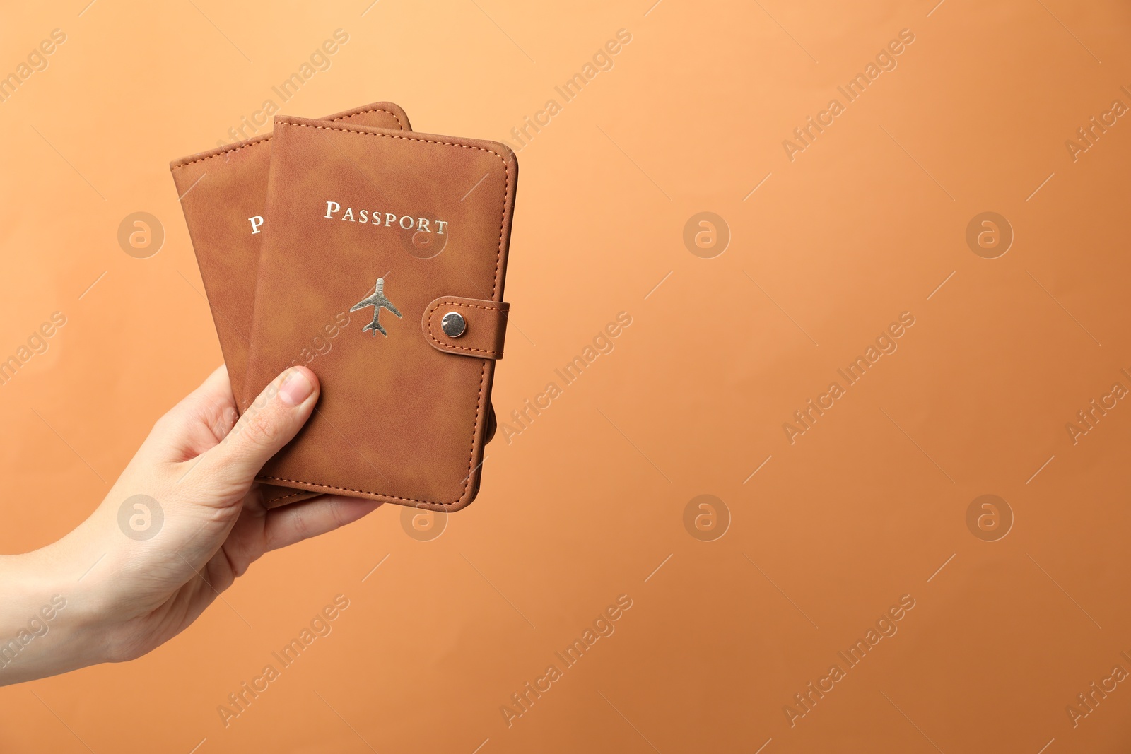 Photo of Woman holding passports in bright covers on orange background, closeup. Space for text