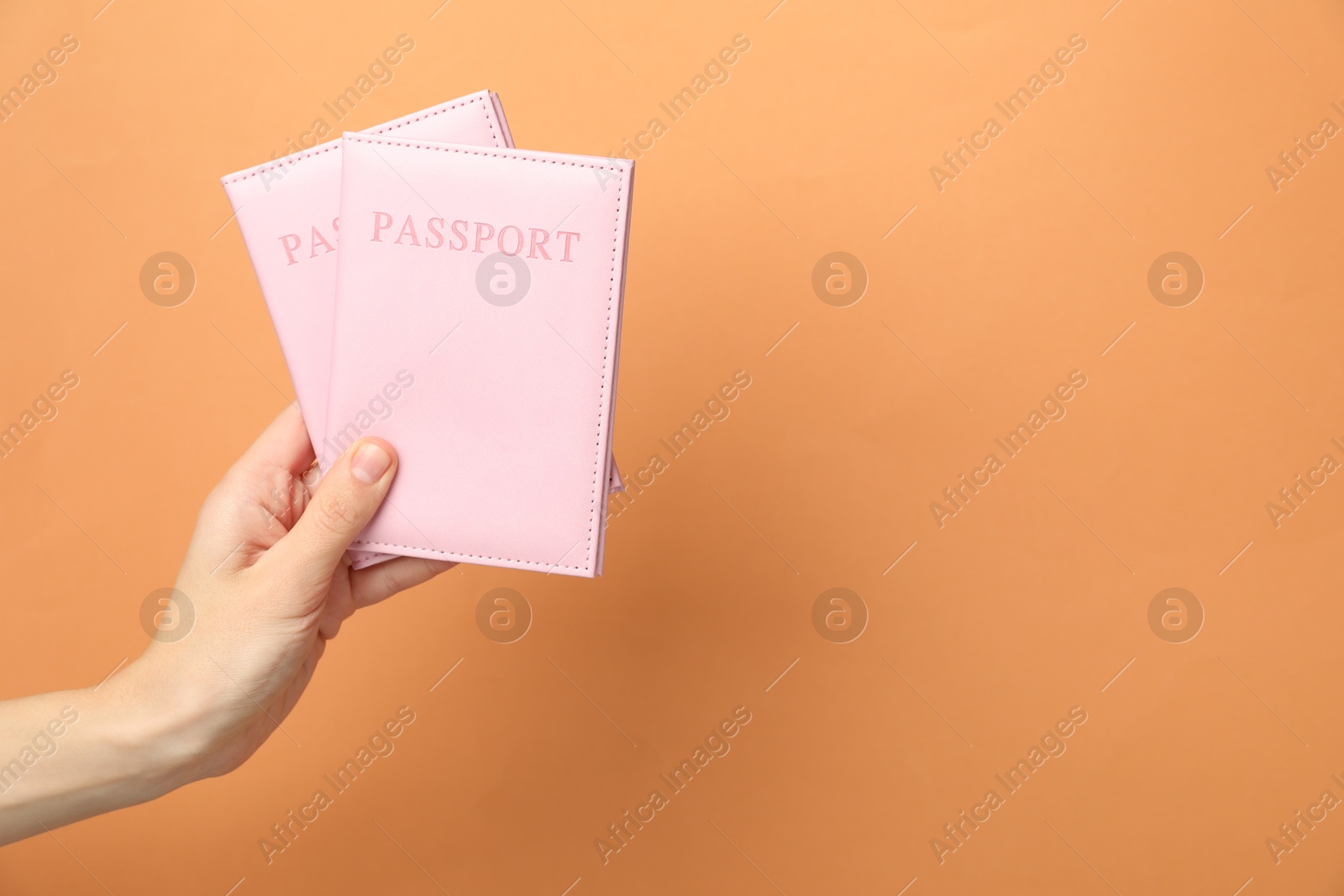 Photo of Woman holding passports in bright covers on orange background, closeup. Space for text