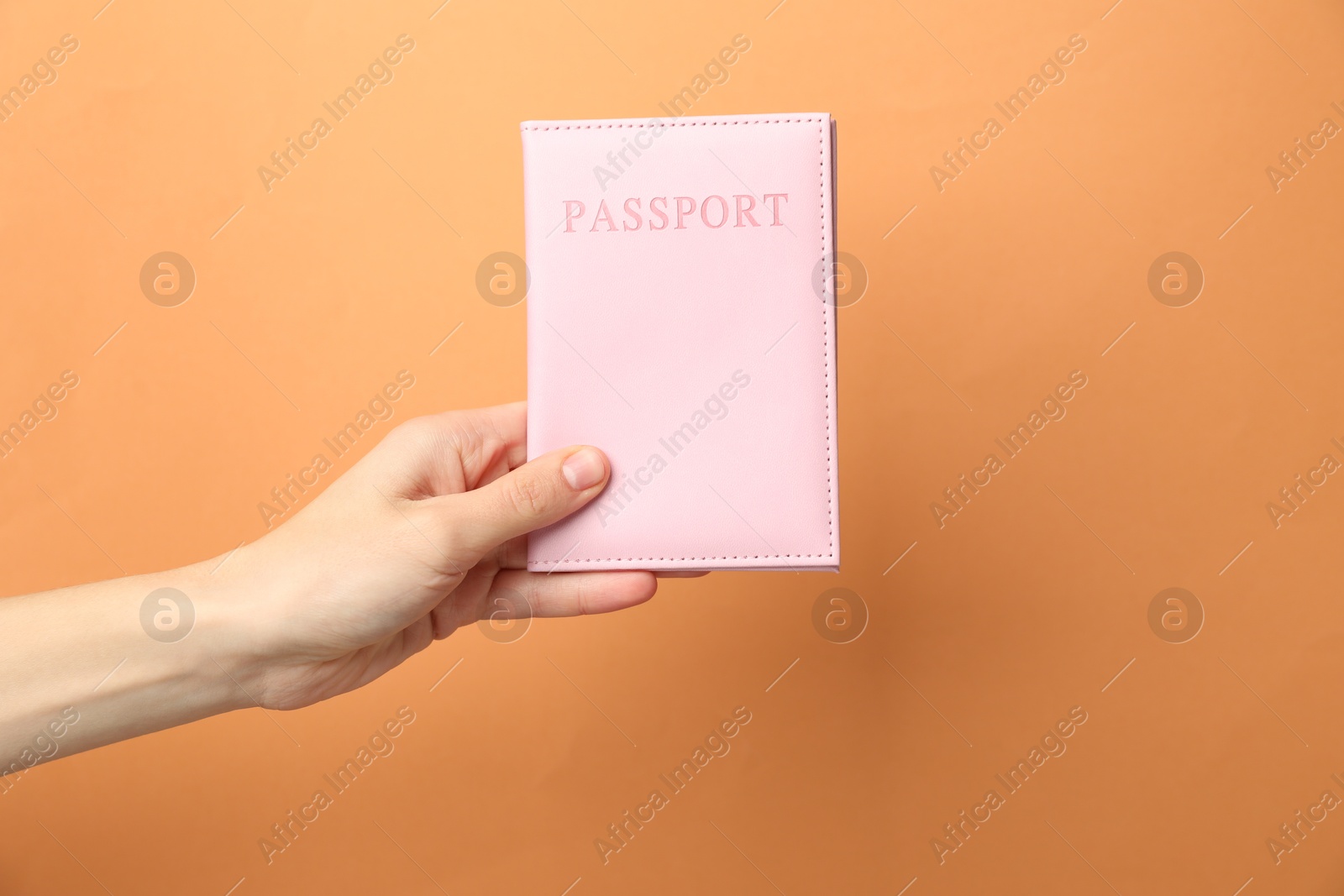 Photo of Woman holding passport in bright cover on orange background, closeup