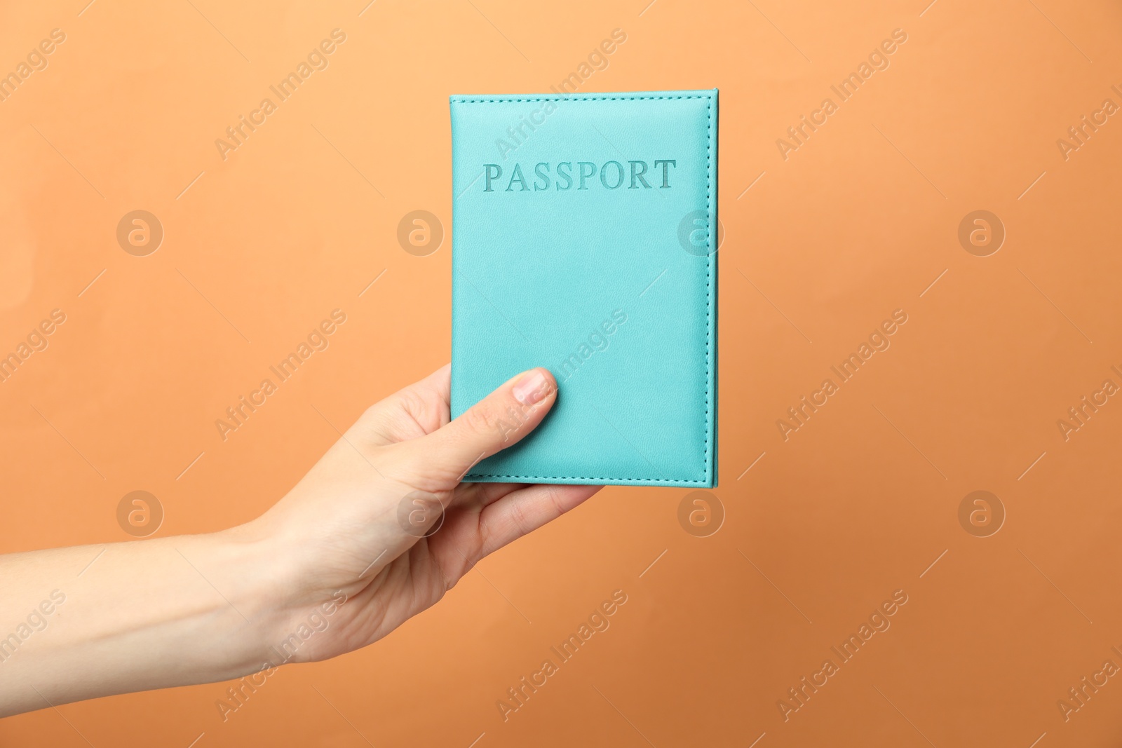 Photo of Woman holding passport in bright cover on orange background, closeup