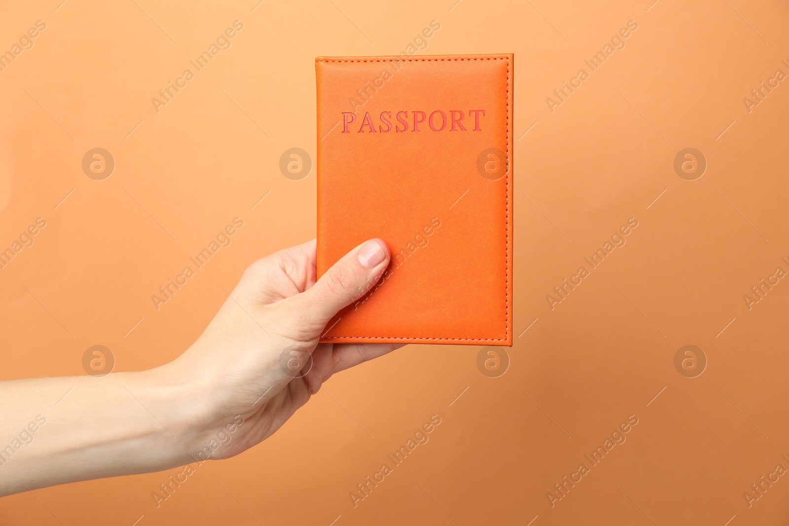 Photo of Woman holding passport in bright cover on orange background, closeup