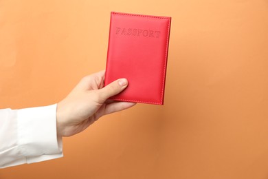 Photo of Woman holding passport in bright cover on orange background, closeup