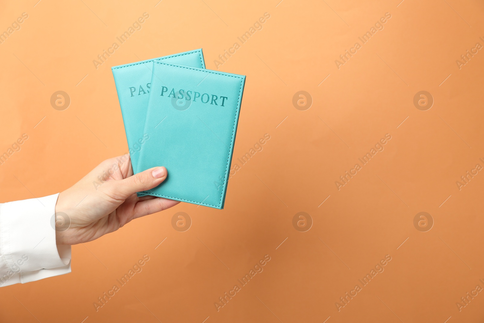 Photo of Woman holding passports in bright covers on orange background, closeup. Space for text