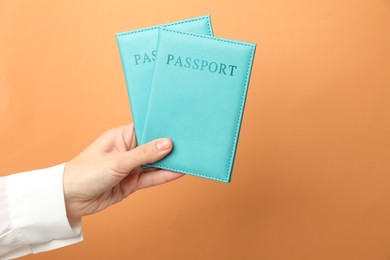 Photo of Woman holding passports in bright covers on orange background, closeup