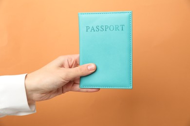 Photo of Woman holding passport in bright cover on orange background, closeup