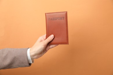 Photo of Woman holding passport in bright cover on orange background, closeup. Space for text