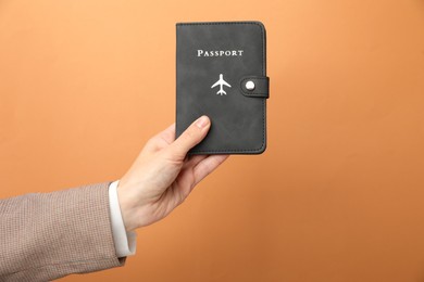 Photo of Woman holding passport in bright cover on orange background, closeup