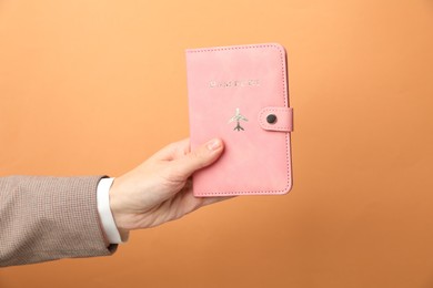 Photo of Woman holding passport in bright cover on orange background, closeup