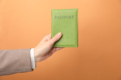 Photo of Woman holding passport in bright cover on orange background, closeup