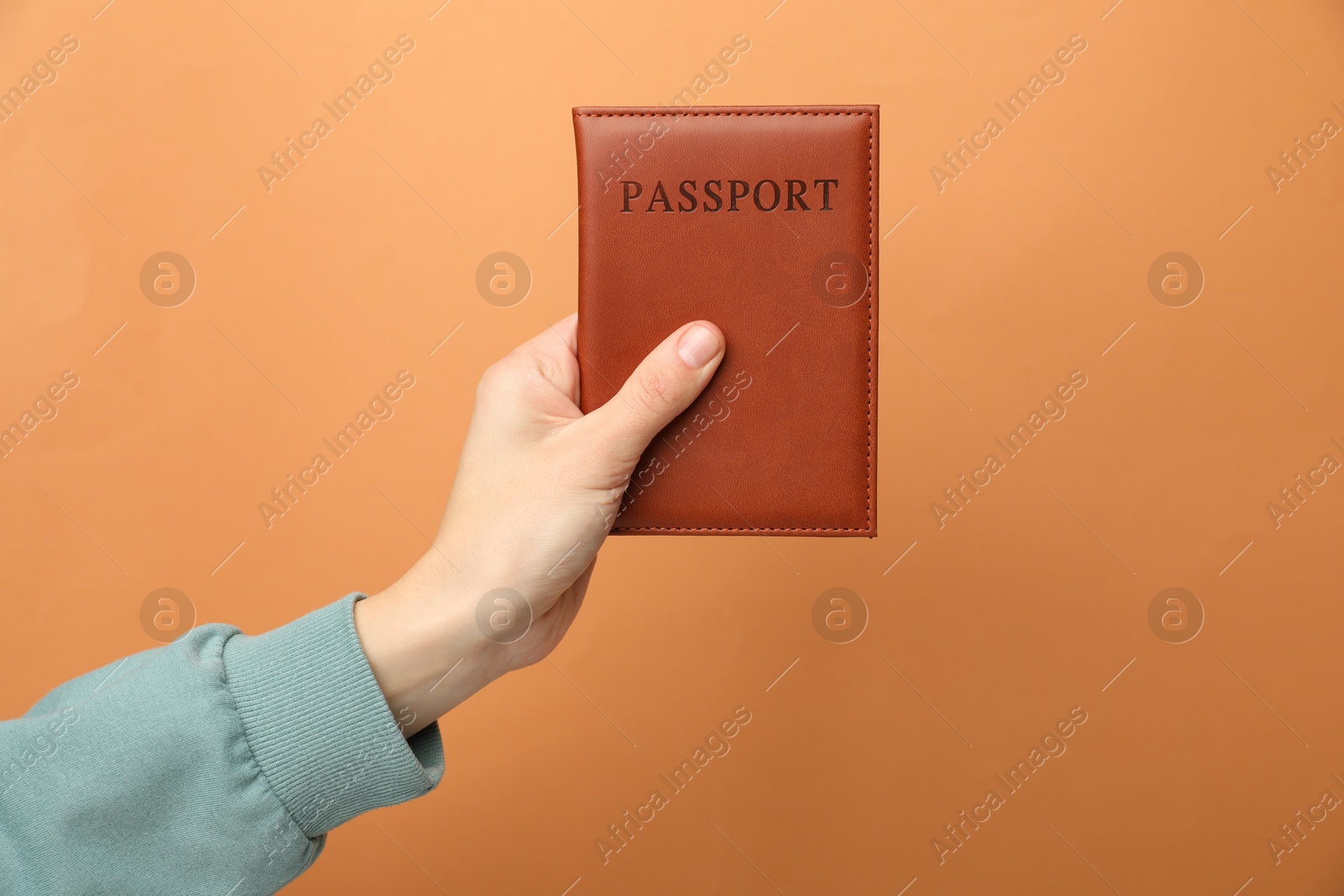 Photo of Woman holding passport in bright cover on orange background, closeup