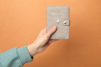 Photo of Woman holding passport in bright cover on orange background, closeup