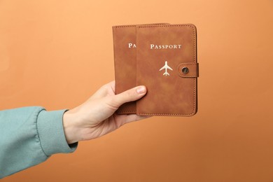 Photo of Woman holding passports in bright covers on orange background, closeup