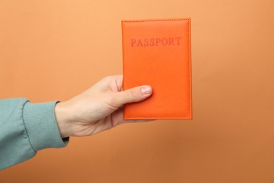 Photo of Woman holding passport in bright cover on orange background, closeup