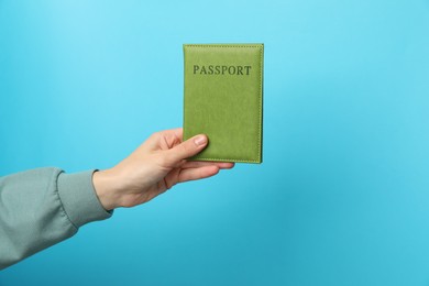 Photo of Woman holding passport in bright cover on light blue background, closeup