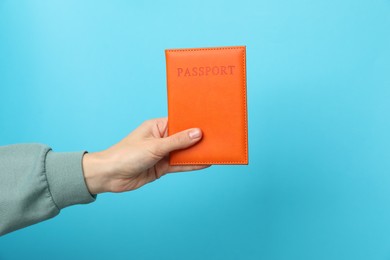 Photo of Woman holding passport in bright cover on light blue background, closeup