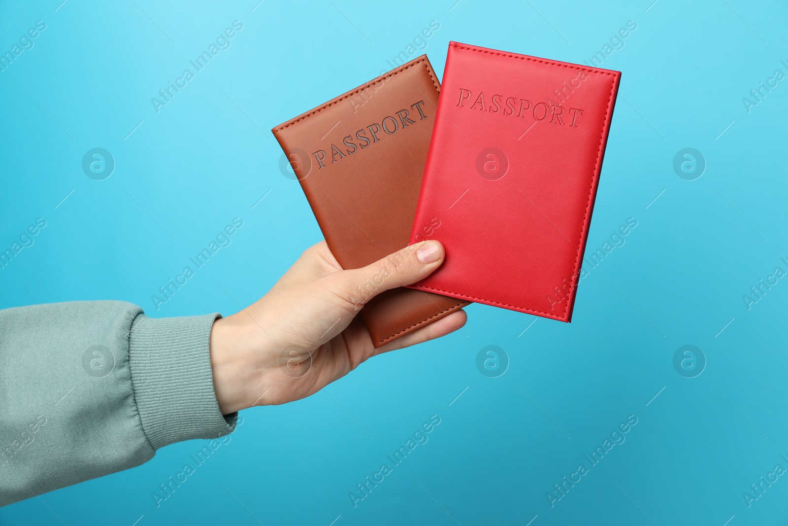 Photo of Woman holding passports in bright covers on light blue background, closeup