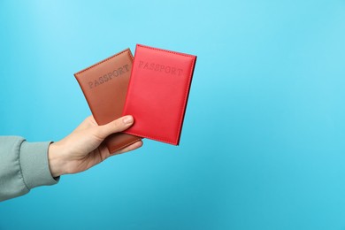 Photo of Woman holding passports in bright covers on light blue background, closeup. Space for text