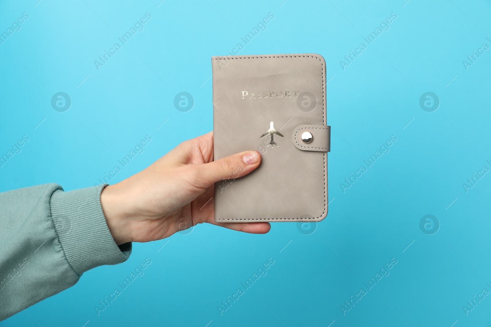 Photo of Woman holding passport in bright cover on light blue background, closeup