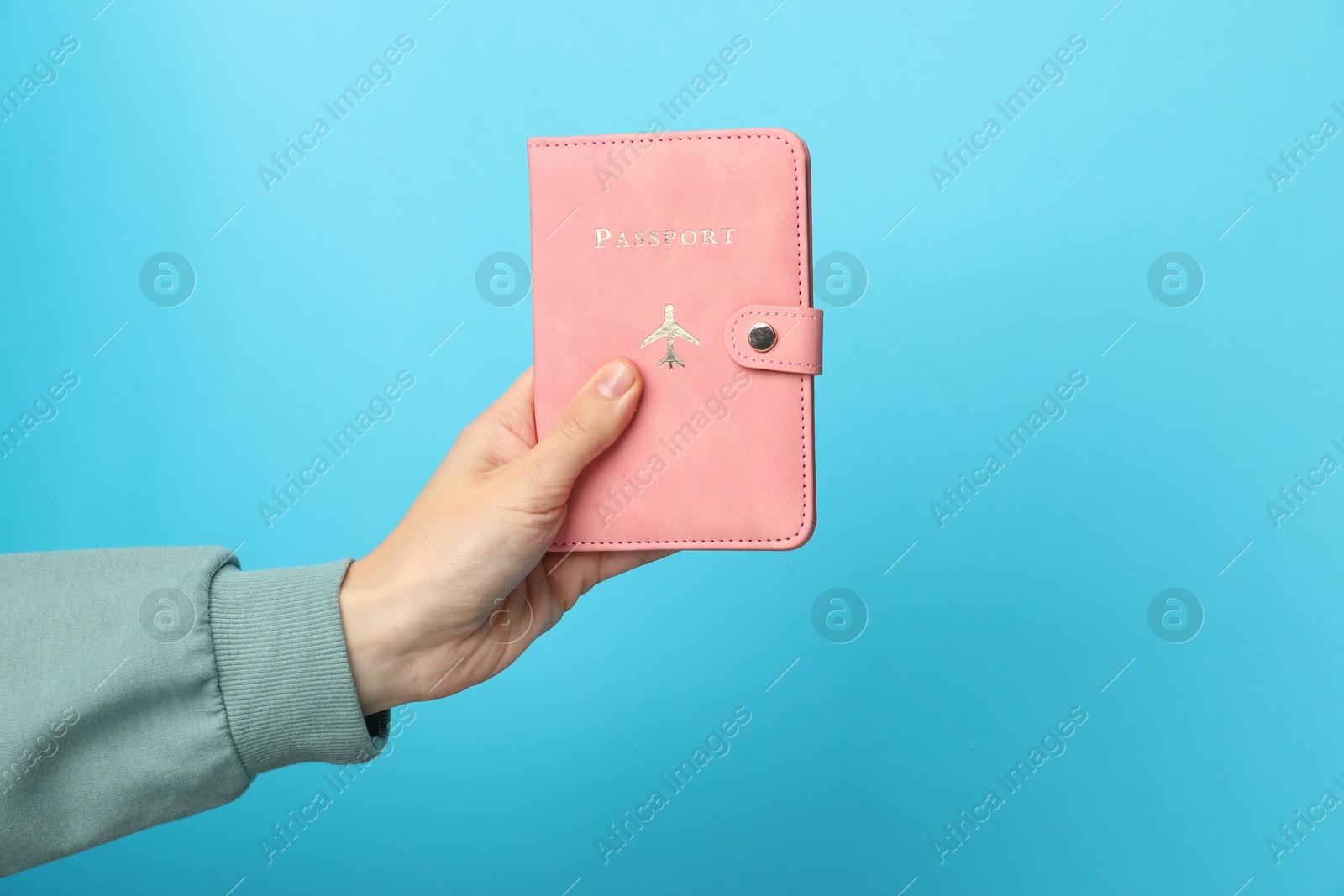 Photo of Woman holding passport in bright cover on light blue background, closeup. Space for text