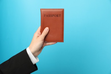 Photo of Woman holding passport in bright cover on light blue background, closeup. Space for text