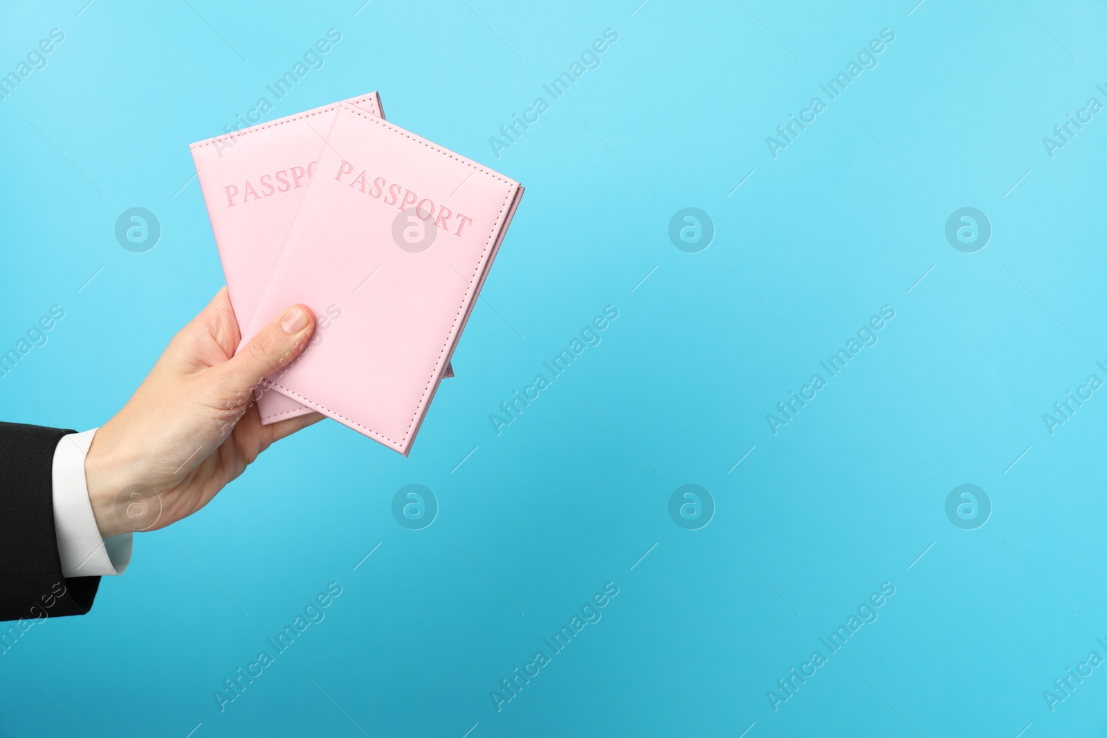 Photo of Woman holding passports in bright covers on light blue background, closeup. Space for text